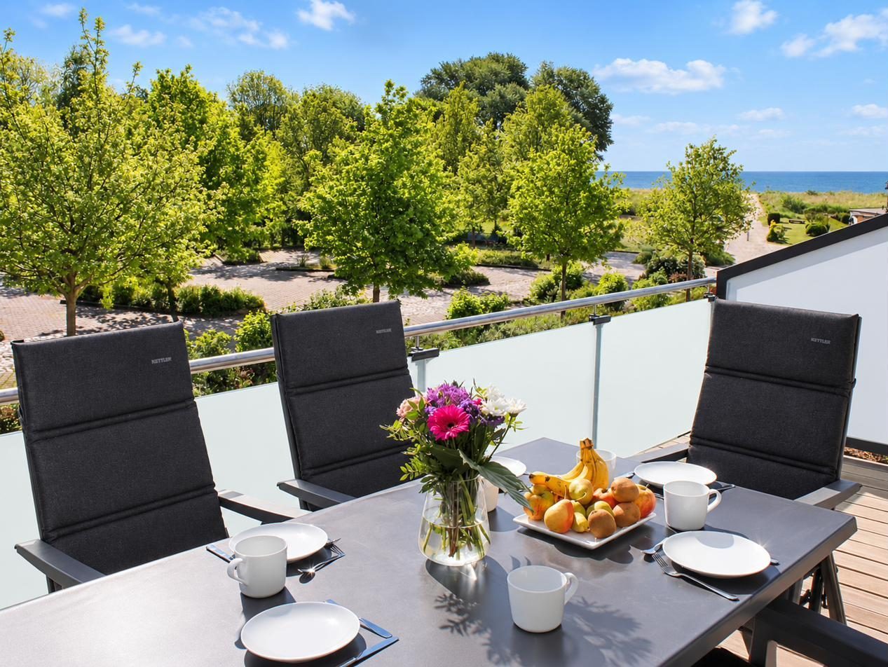 Gedeckter Frühstückstisch auf dem Balkon, dahinter Bäume und die Ostsee